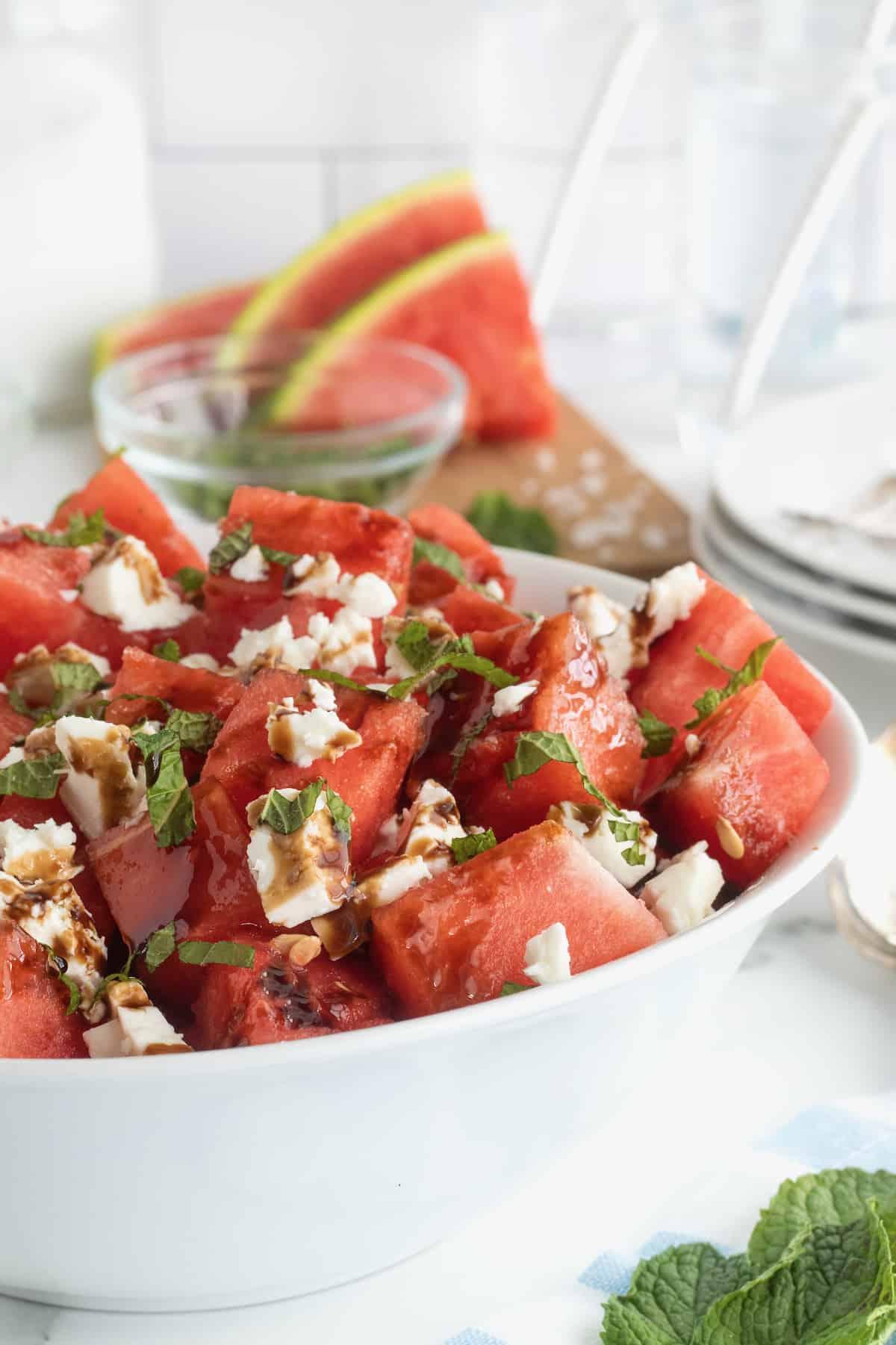 A vibrant summer salad with watermelon, feta cheese, mint, and a balsamic glaze drizzled over it.
