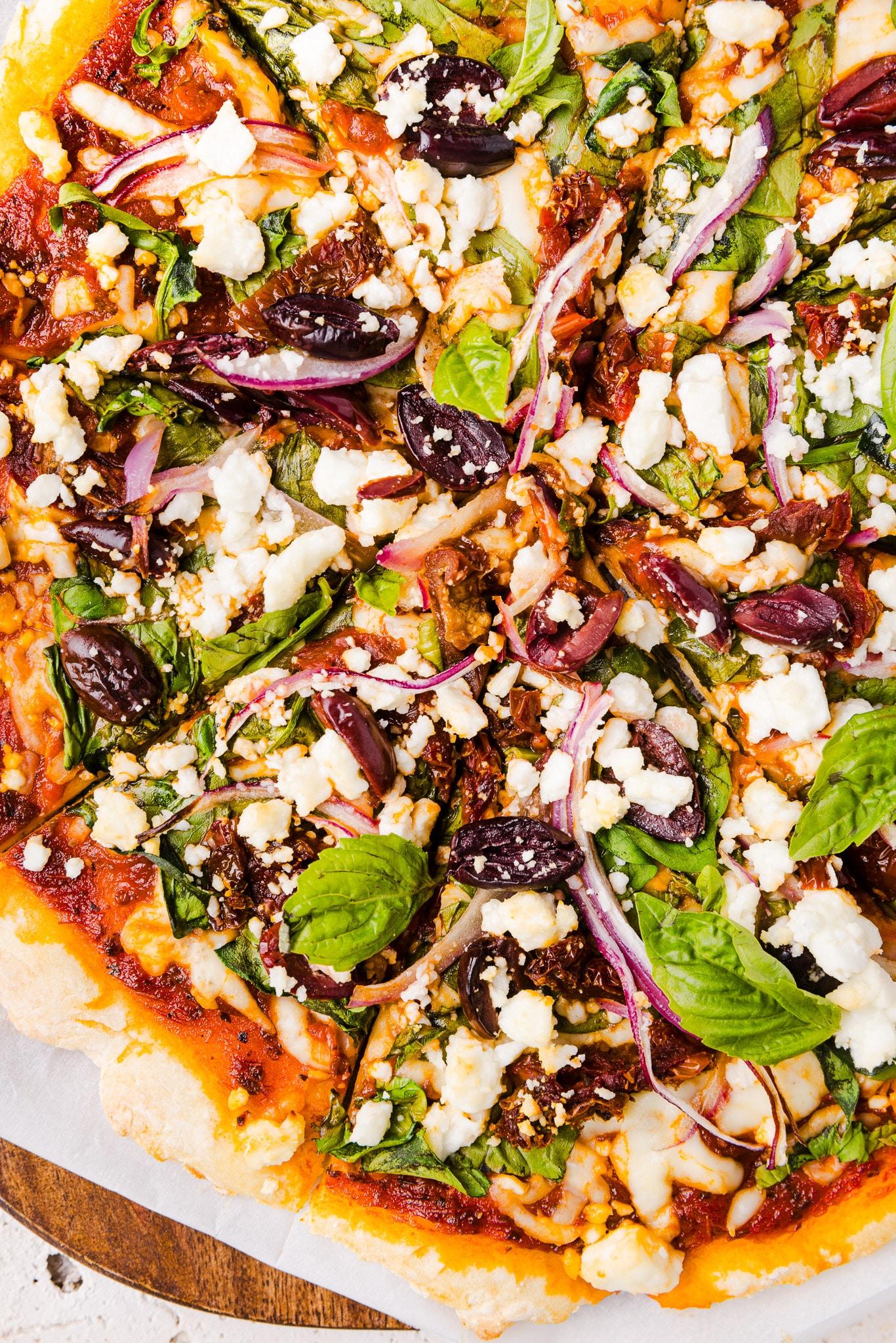 Close-up shot of a spinach, feta, and sun-dried tomato pizza, with the crust slightly charred around the edges.