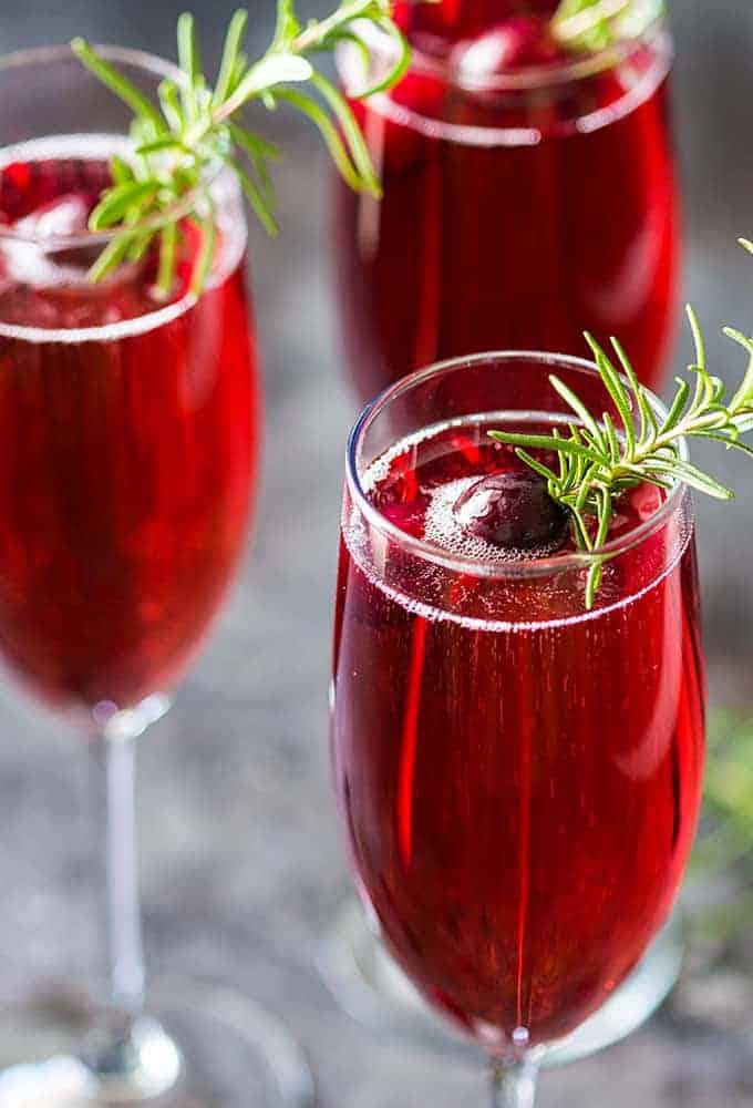 Close-up of two cranberry rosemary mimosas in champagne flutes garnished with rosemary sprigs