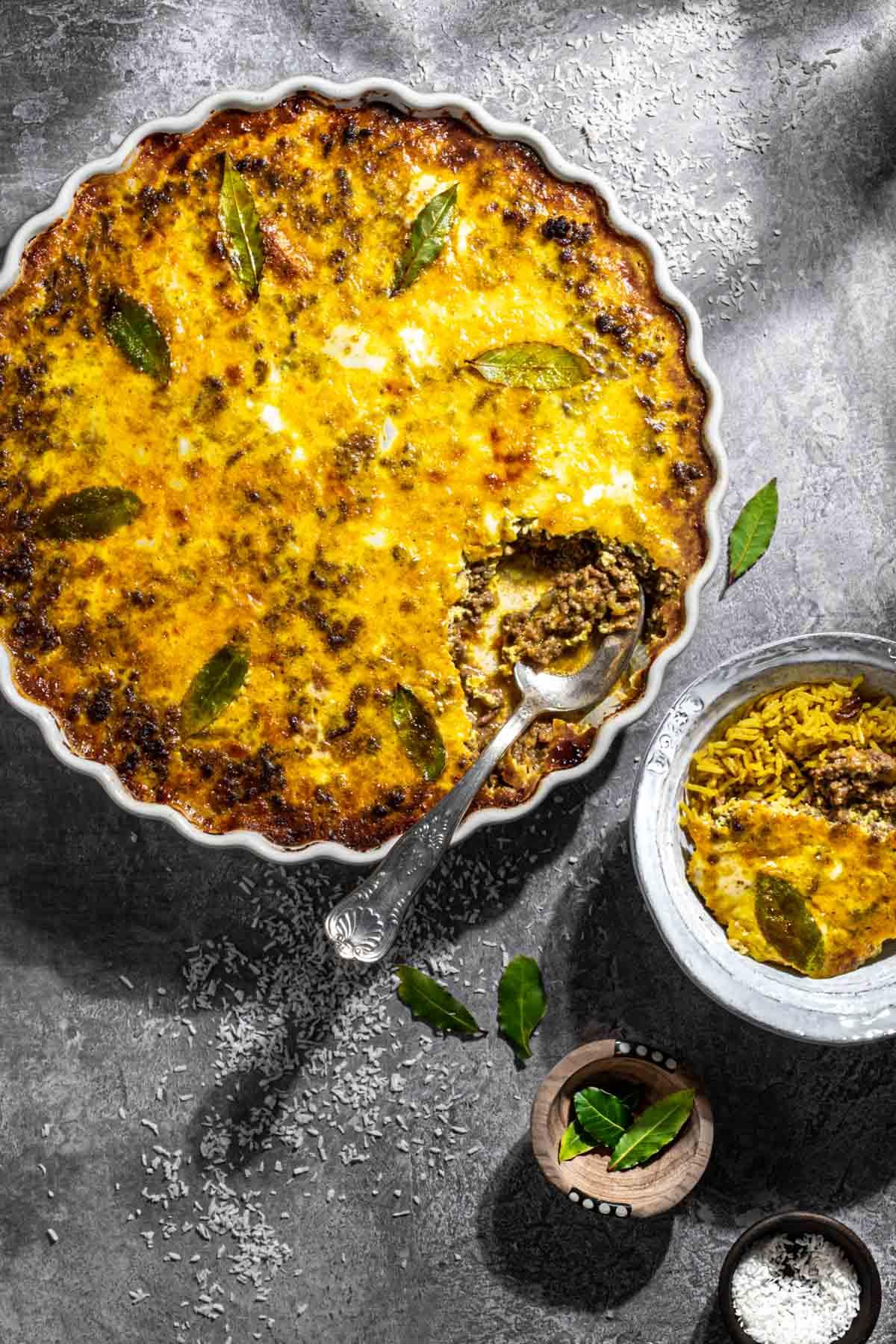 Close up shot of a golden brown Bobotie casserole topped with crispy fried onions, showcasing the kimchi within the mixture