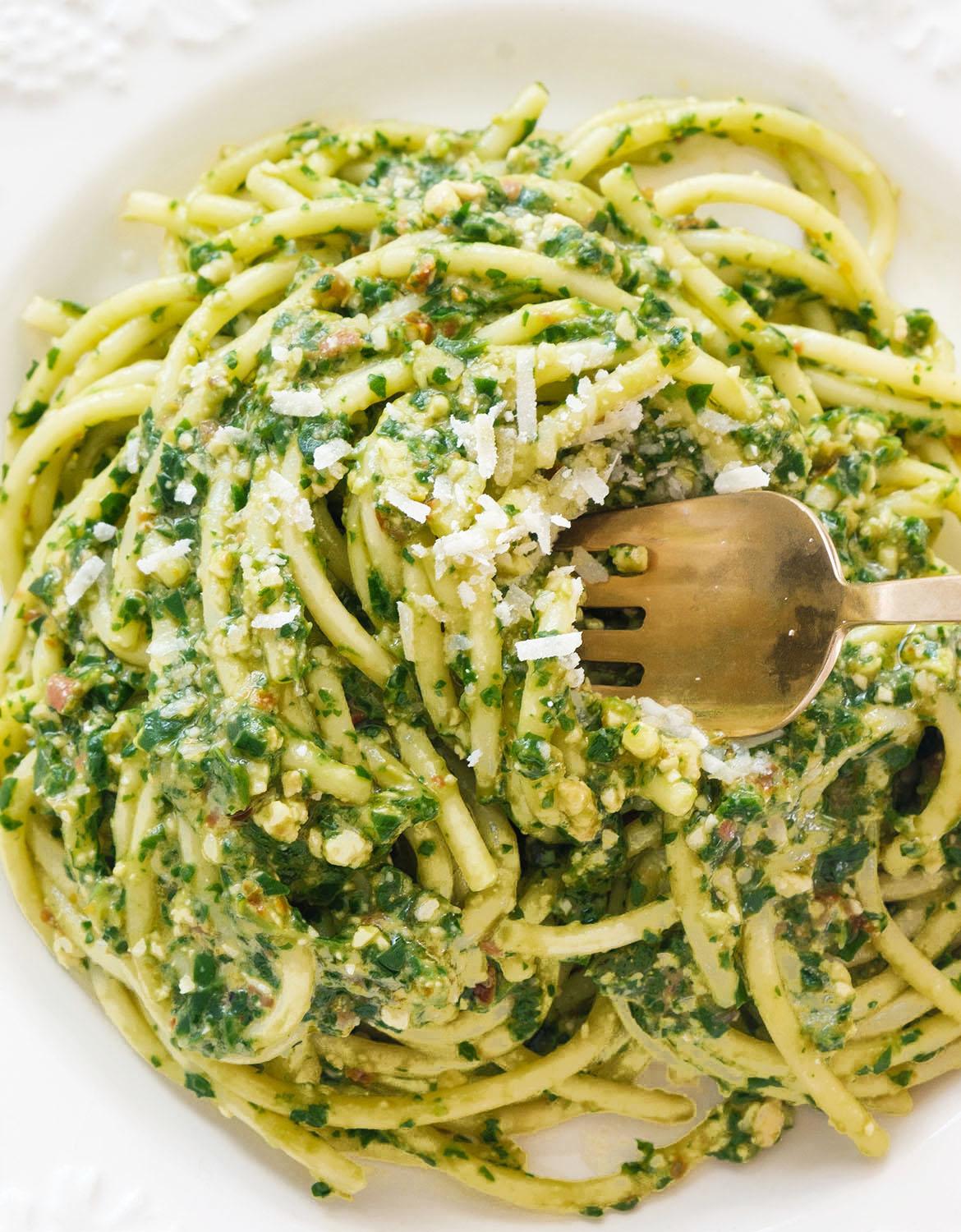 Close-up shot of a plate of creamy green pasta with arugula and Parmesan cheese