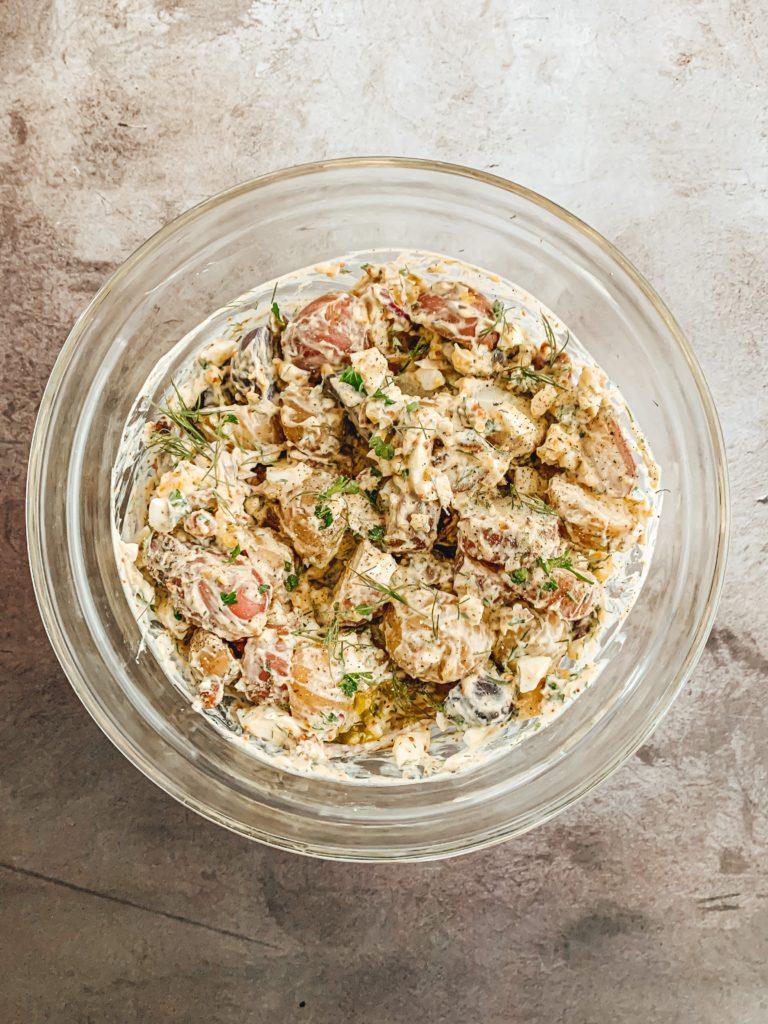 A rustic wooden bowl filled with creamy potato salad, garnished with fresh herbs