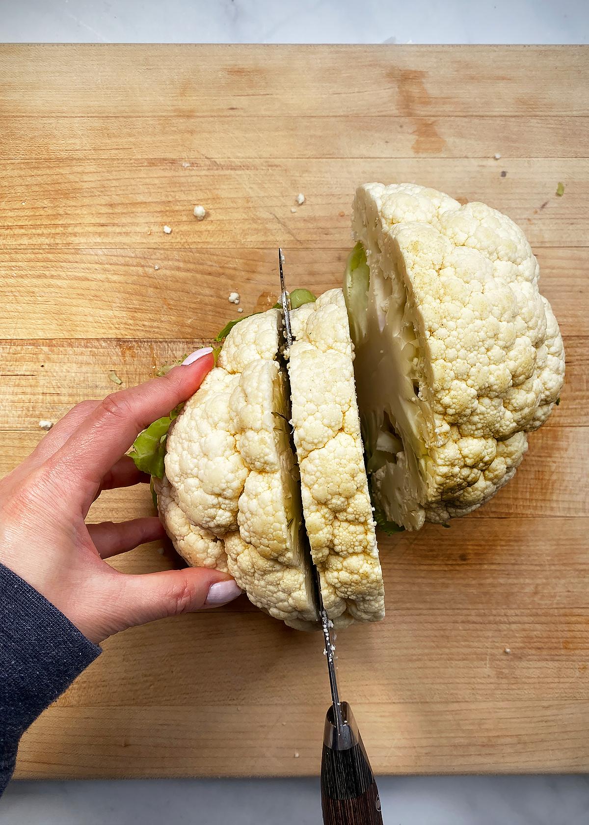 raw cauliflower head being sliced into steaks