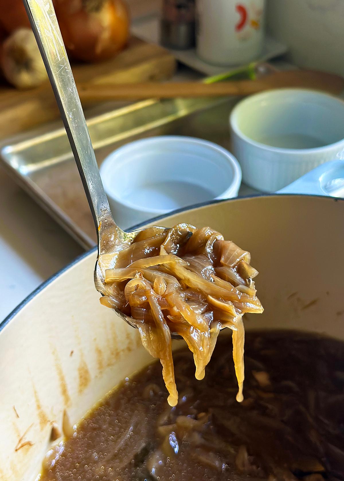 A person ladling the French onion soup into oven-safe bowls.