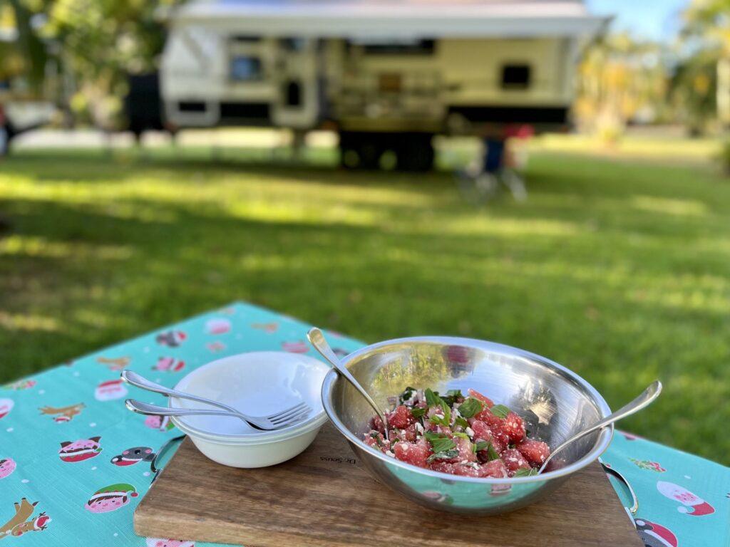 A bowl of watermelon salad being served outdoors on a picnic table.