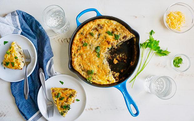A beautifully set table with a Kale and Sausage Frittata as the centerpiece, alongside other breakfast items.