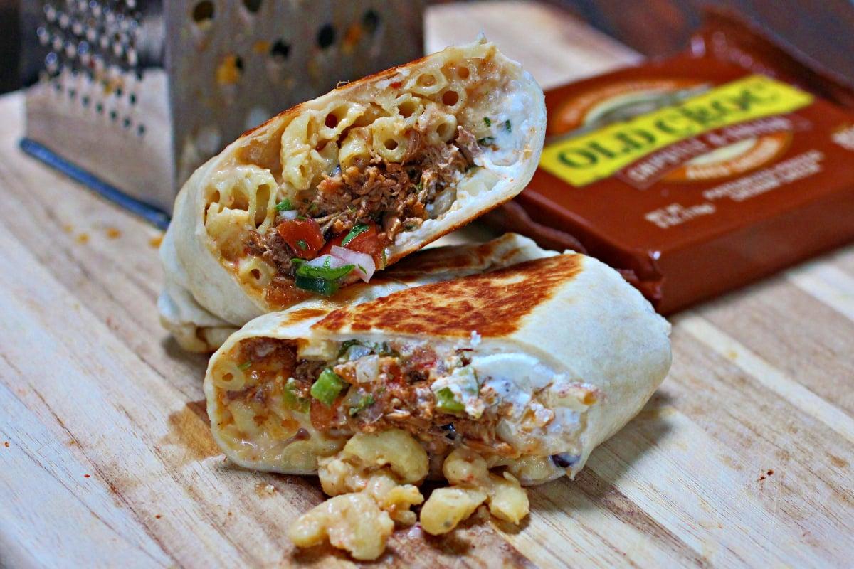 a hand holding a Mac and Cheese Burrito Bowl, ready to take a bite