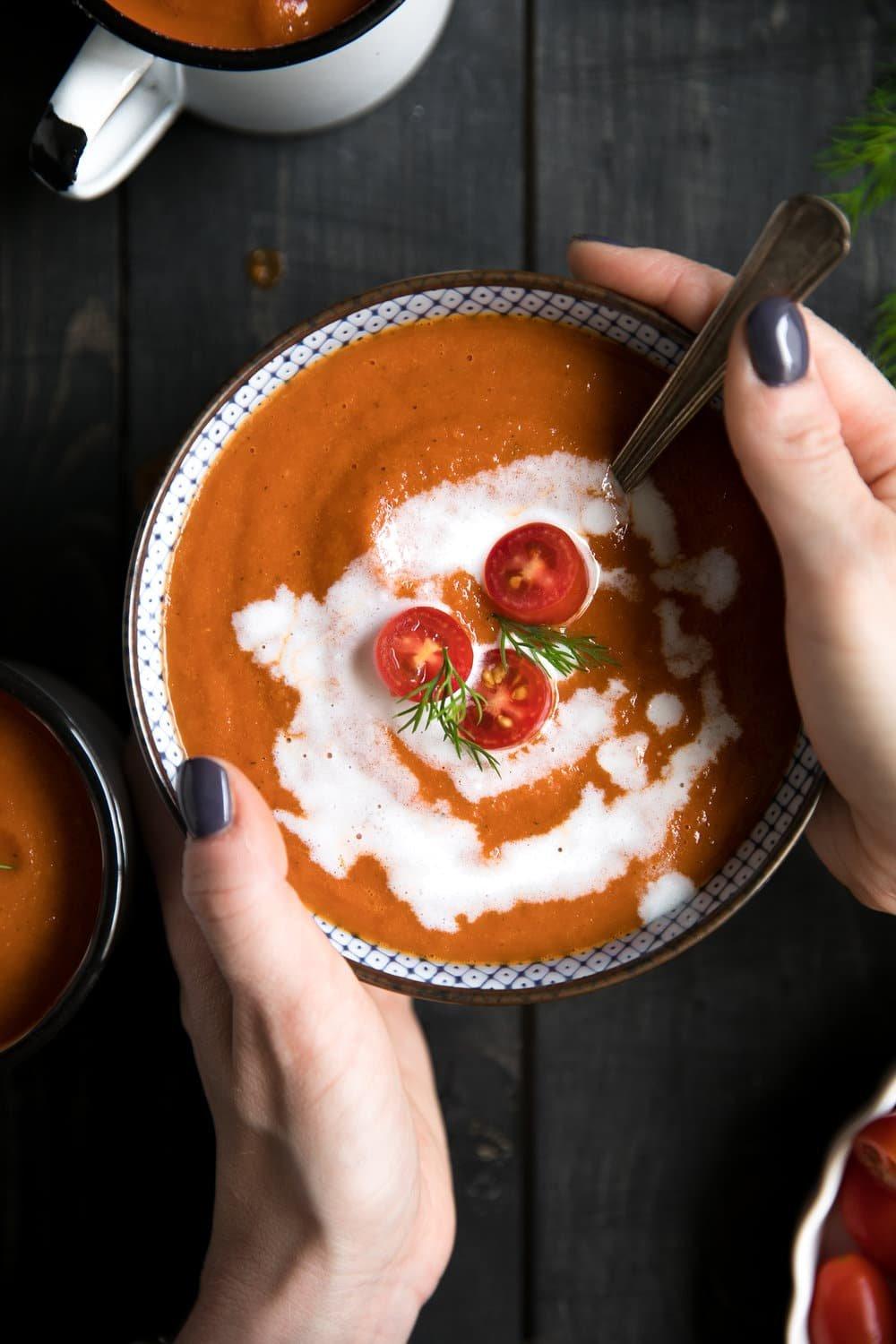 close-up shot of someone ladling roasted red pepper tomato soup into a bowl