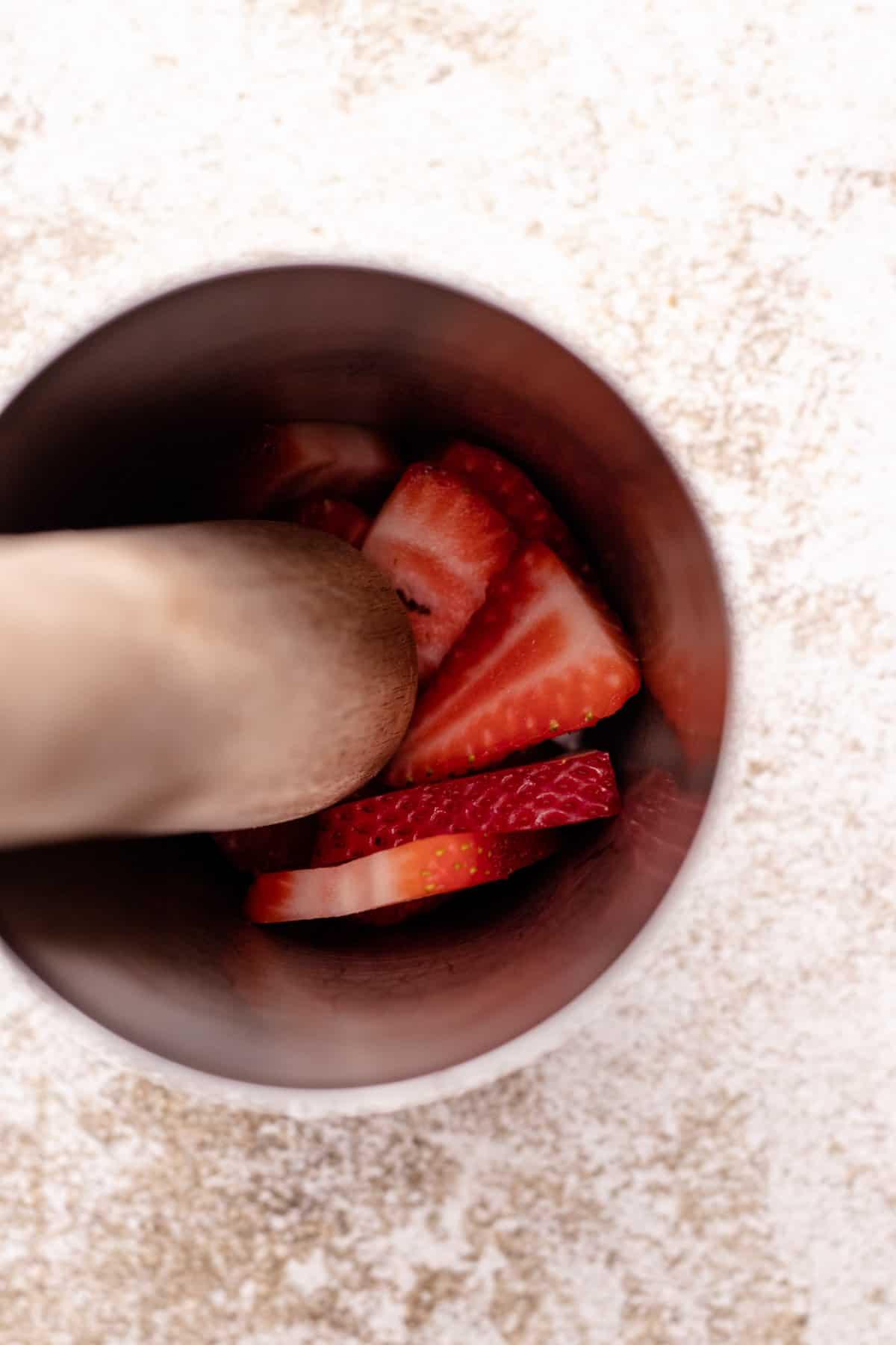 Close up of hands muddling strawberries and adding other ingredients to a cocktail shaker