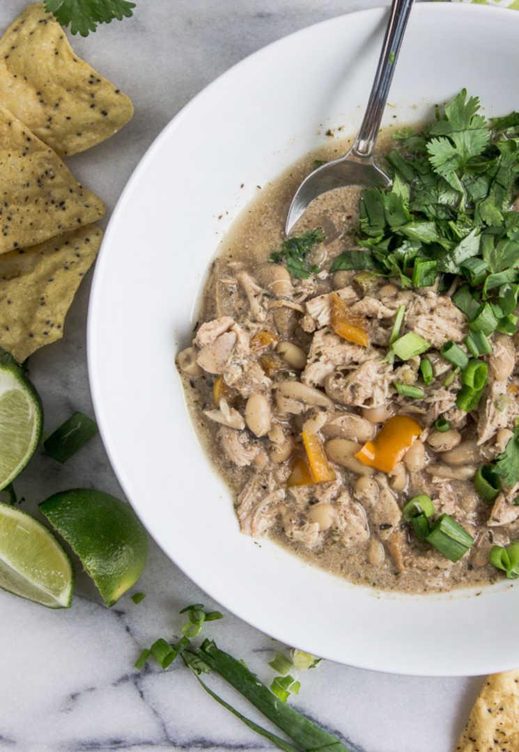 A rustic bowl of jerk chicken chili with toasted pepitas on top, garnished with cilantro