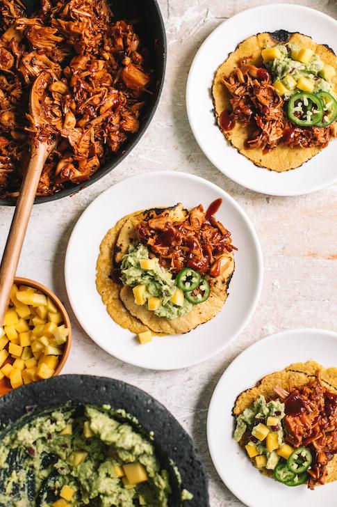 Close-up shot of two BBQ jackfruit arepas topped with chipotle aioli, garnished with cilantro, against a rustic wooden background
