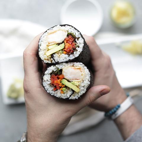 A person smiling while preparing sushi burrito ingredients