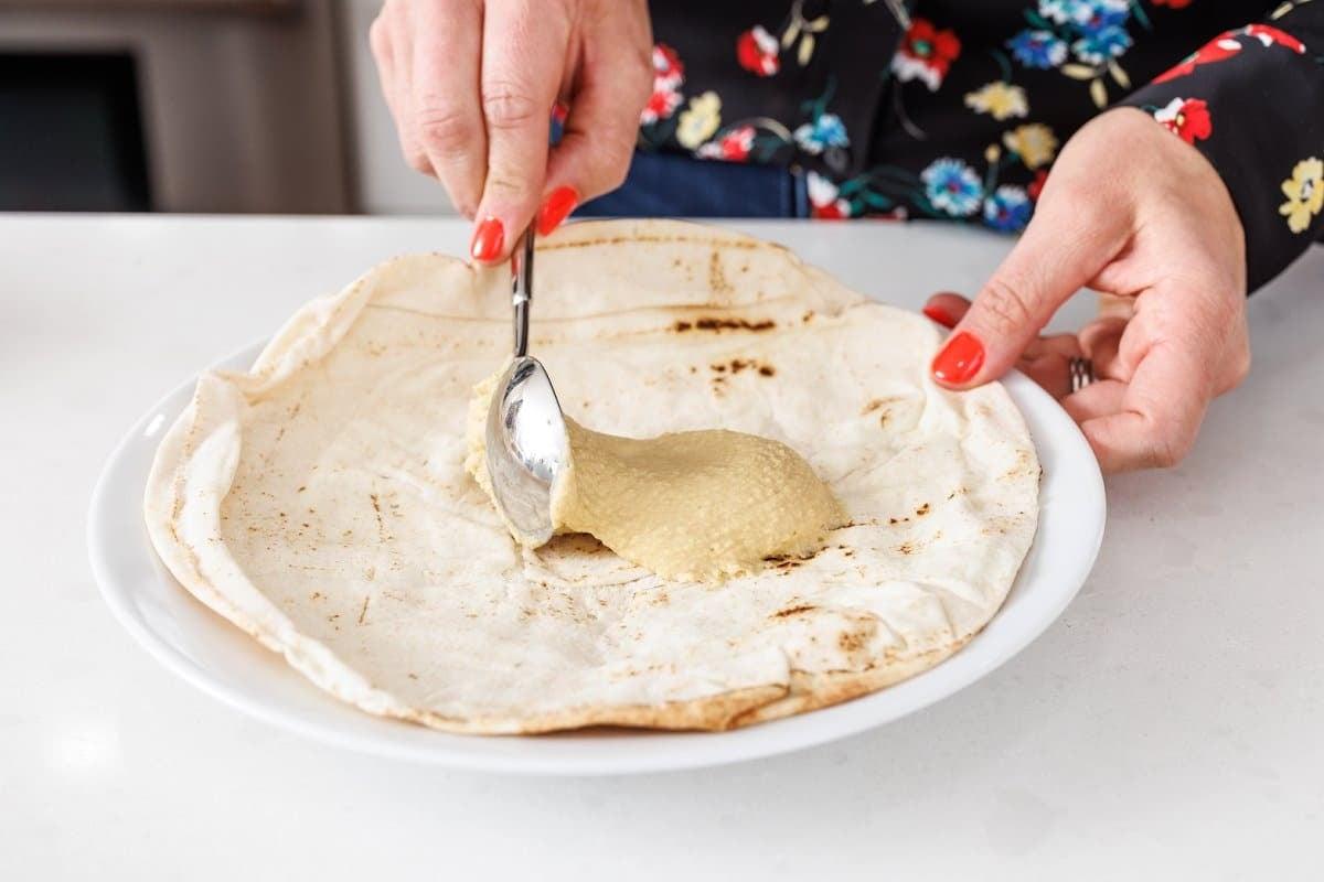 Someone spreading hummus on pita bread.