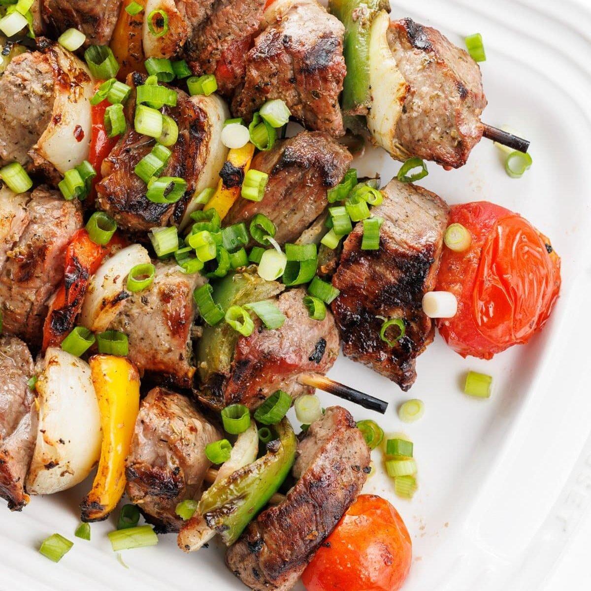 Close-up shot of delicious beef souvlaki skewers with red onion marmalade drizzled on top, garnished with fresh herbs.