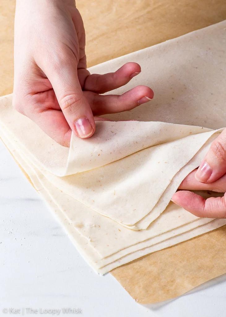 Close up of hands carefully layering phyllo dough for baklava