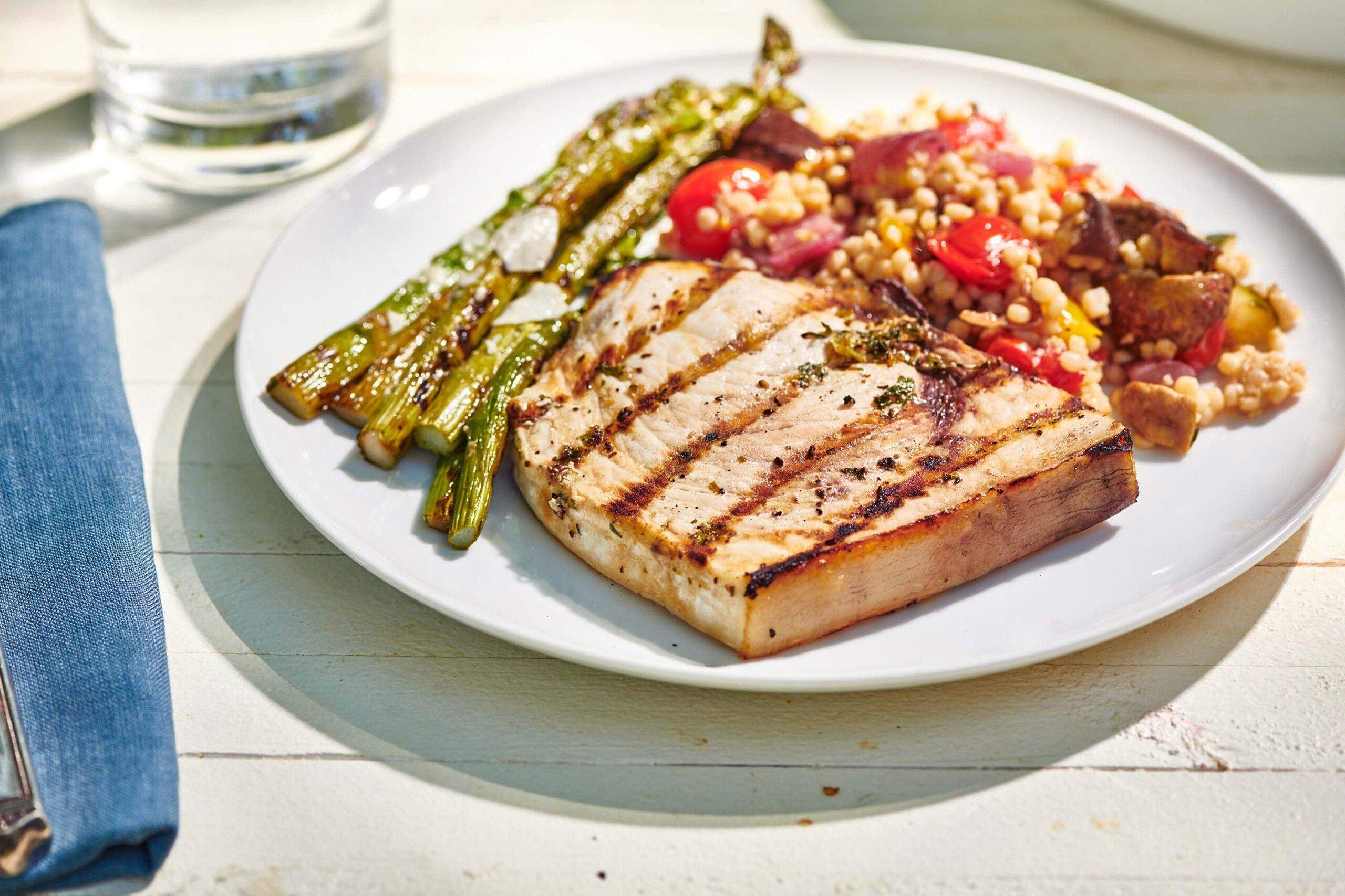 A picturesque coastal setting with a focus on a plate of grilled swordfish