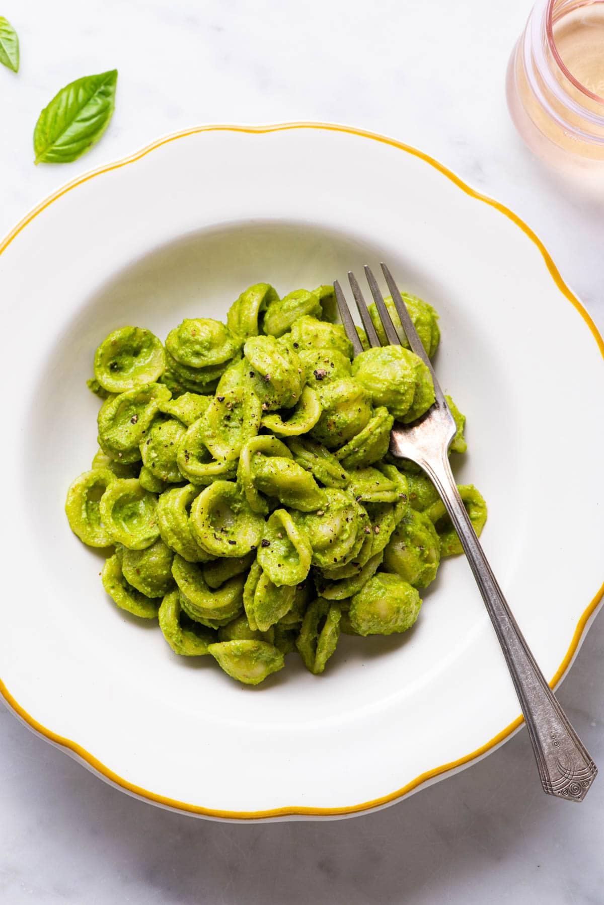 A person happily eating a plate of pasta with spinach pesto sauce