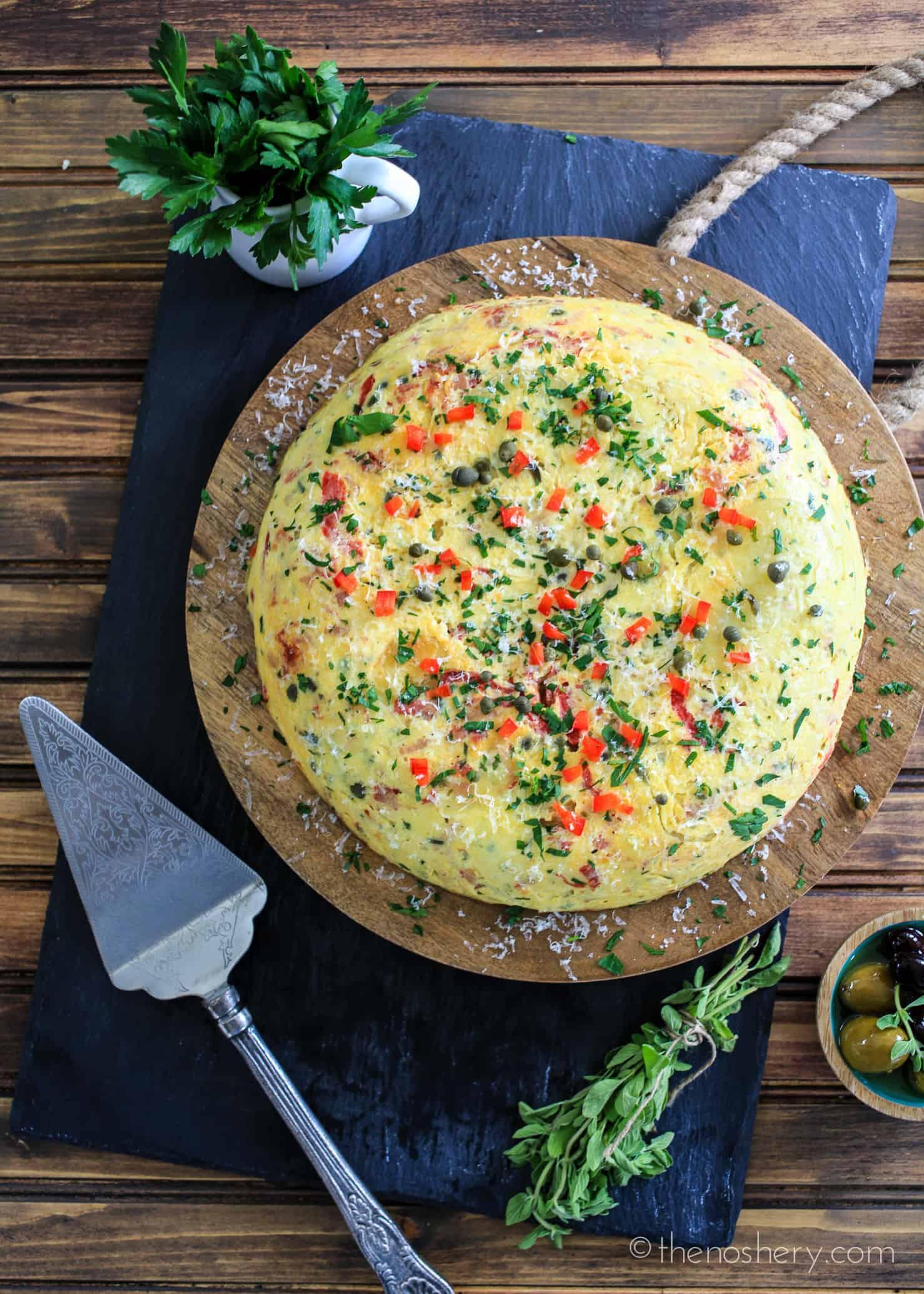 Overhead shot of a Tortilla Española cooking in a skillet, with piquillo peppers and Manchego cheese visible on top