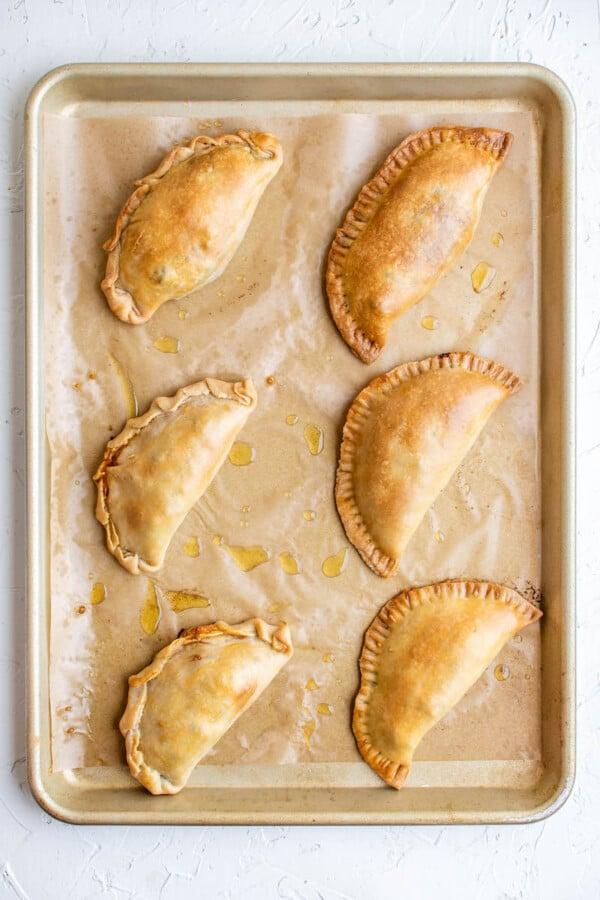 Close-up shot of golden brown beef and cheese empanadas on a baking sheet
