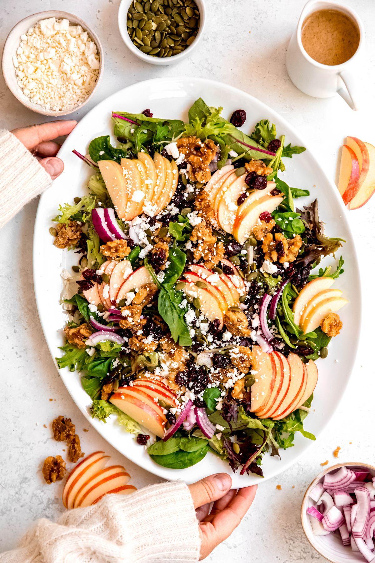 overhead shot of a large wooden bowl filled with apple walnut salad, honey drizzled over