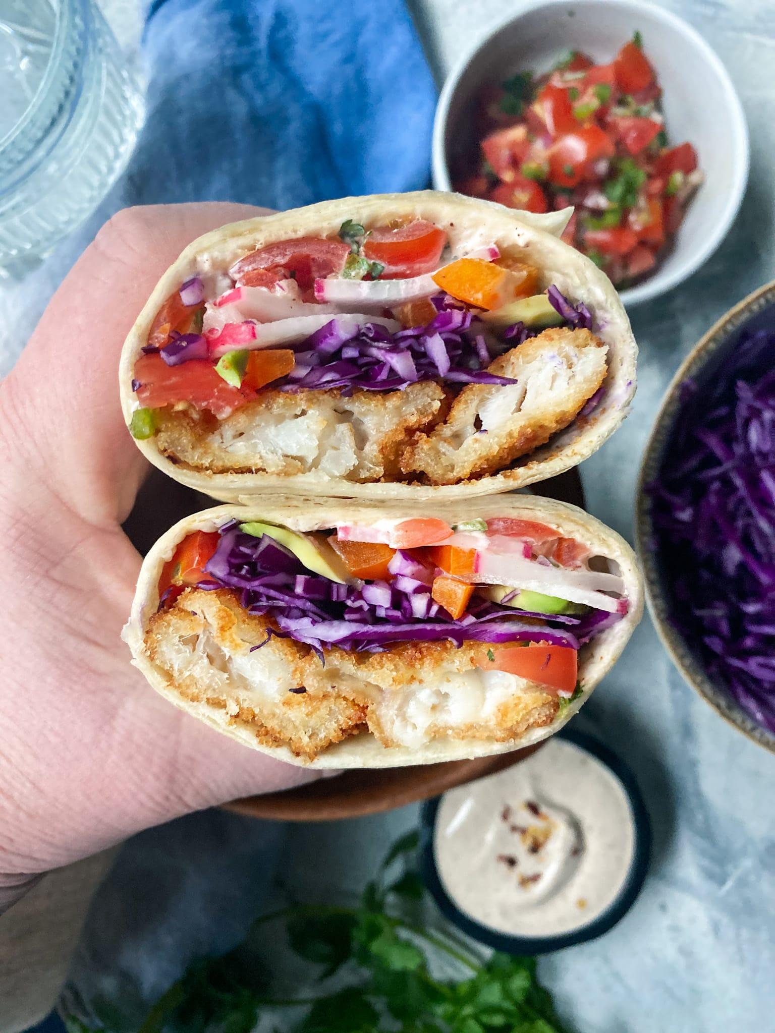 close-up shot of the Baja sauce being drizzled over the fish and cabbage inside the burrito