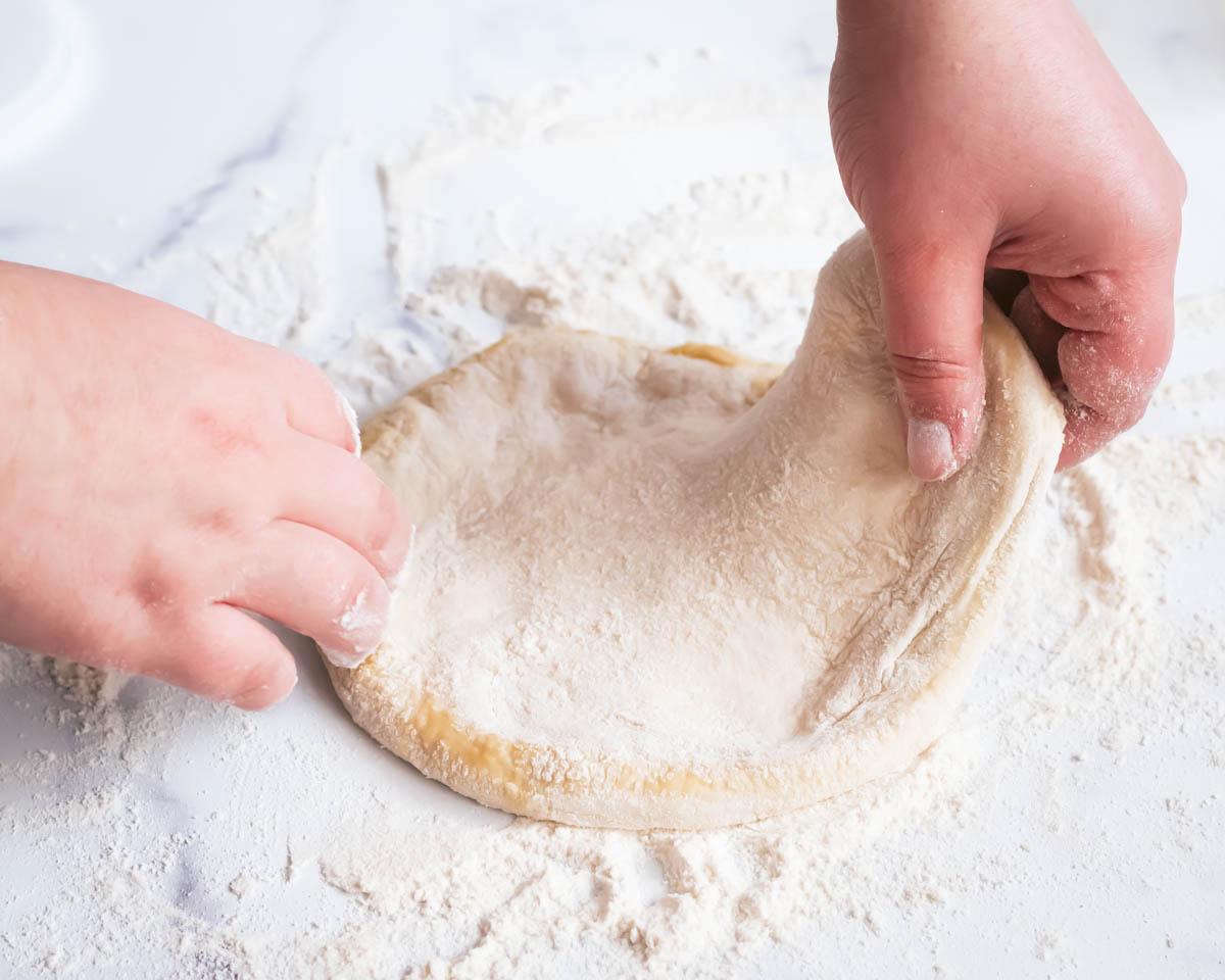 person stretching pizza dough