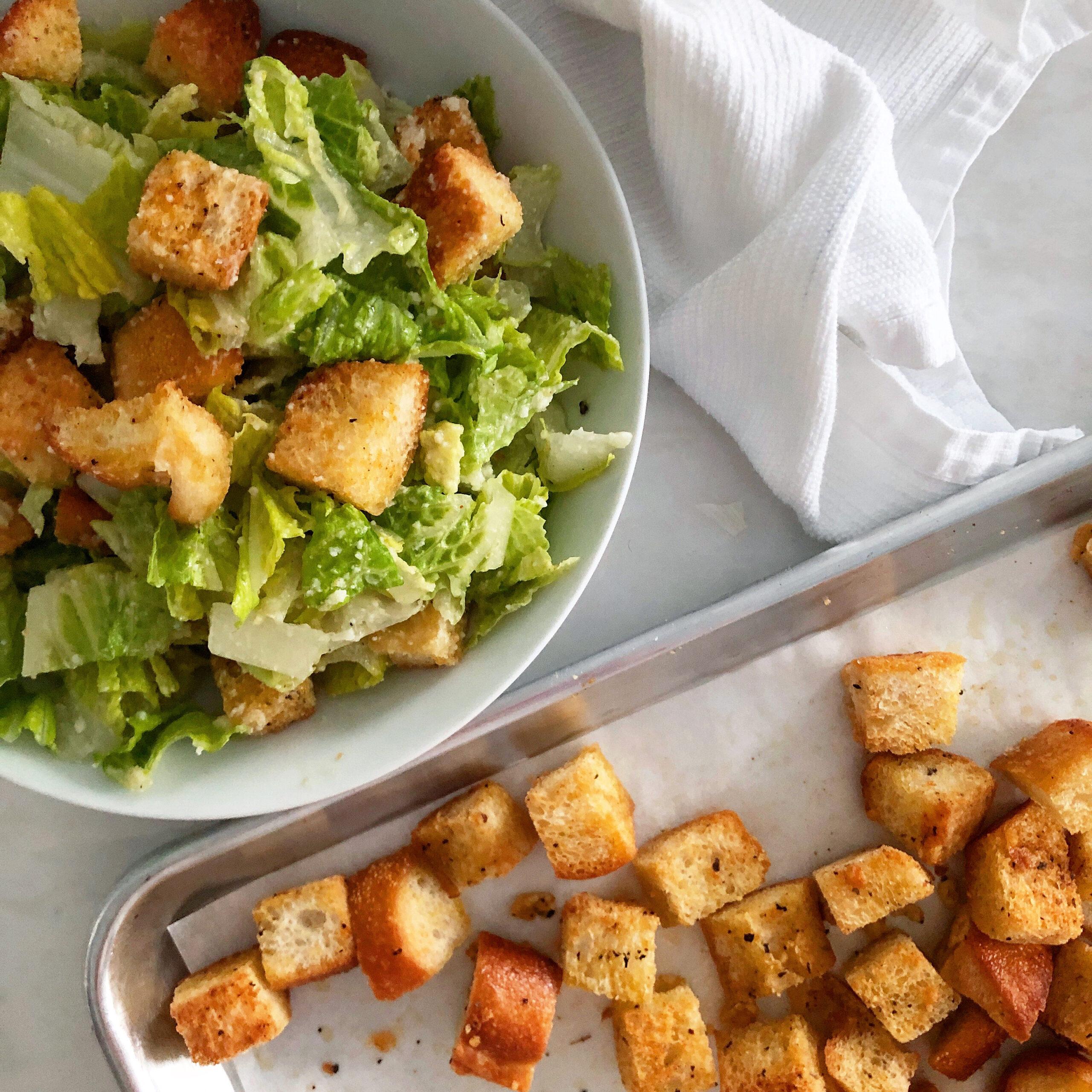 A vibrant Caesar salad with homemade croutons in a large bowl, garnished with parmesan cheese and herbs.