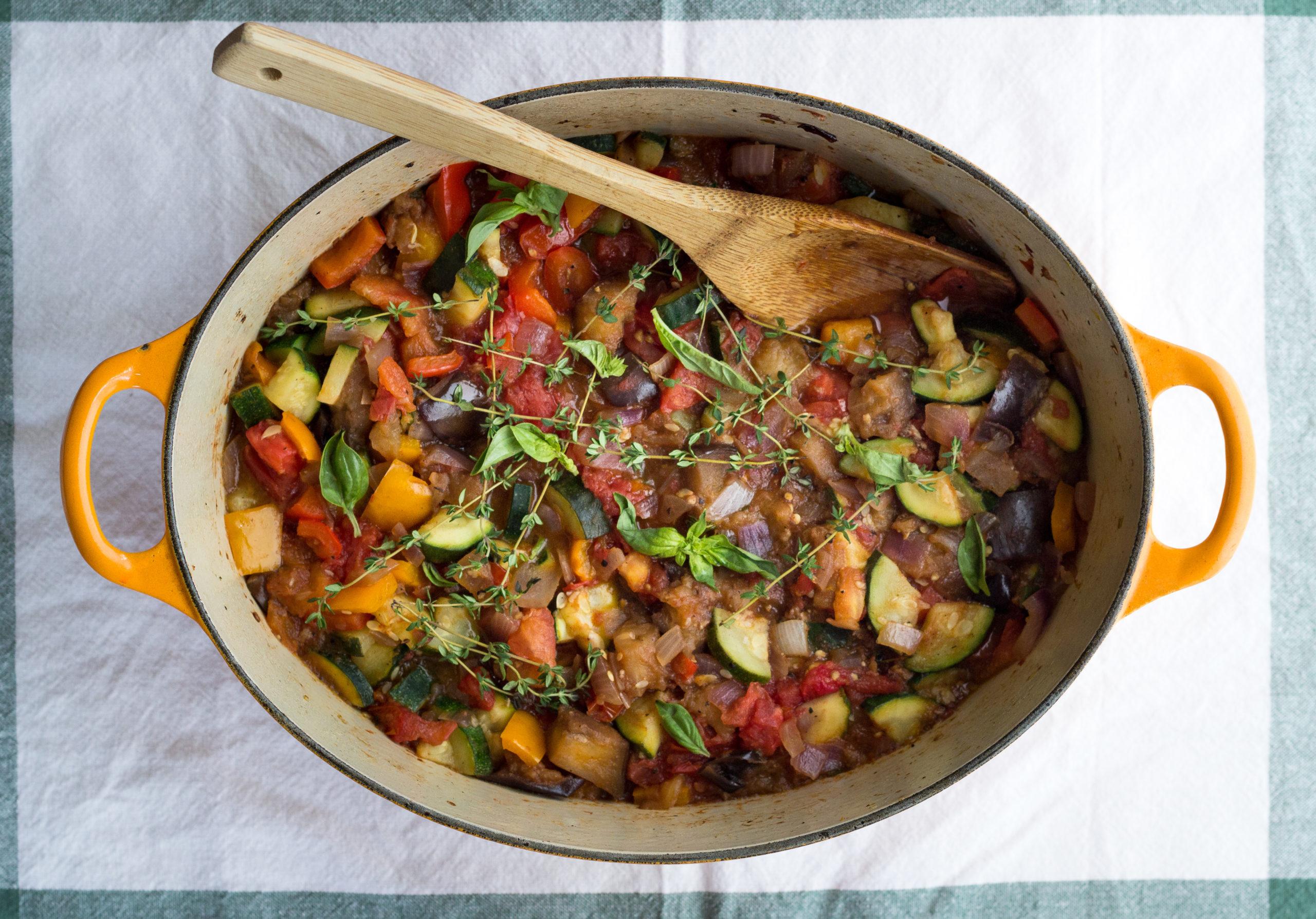 Overhead shot of a rustic kitchen table with ratatouille in a bowl and chocolate mousse in a glass, side by side