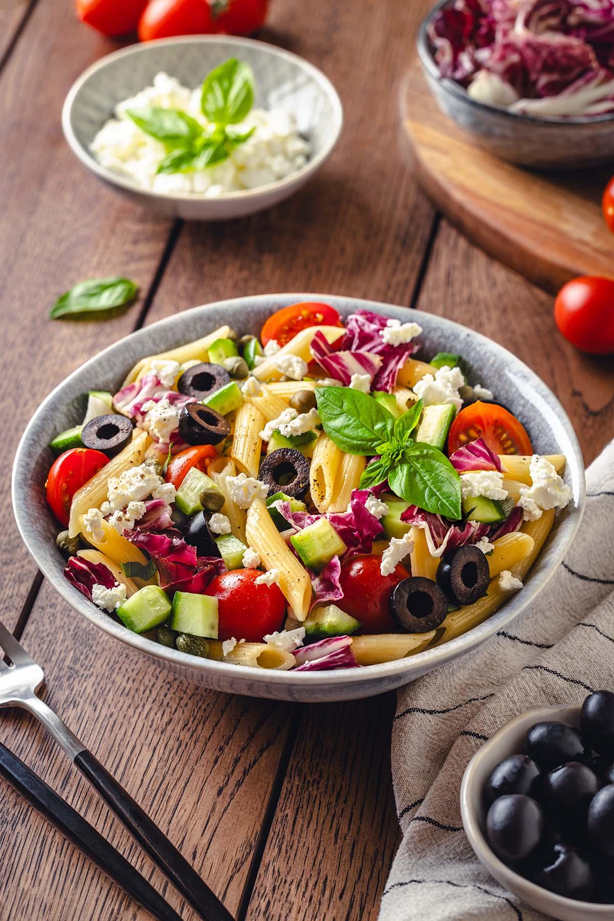 A bowl of the Italian pasta salad served on a rustic wooden table, garnished with fresh basil.
