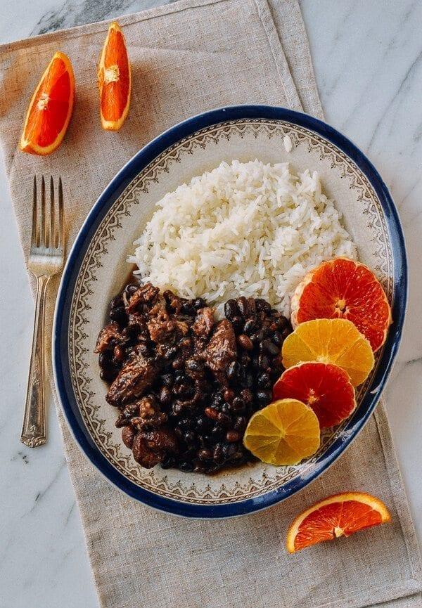 A steaming pot of Brazilian Feijoada with traditional sides like rice, farofa, and orange slices