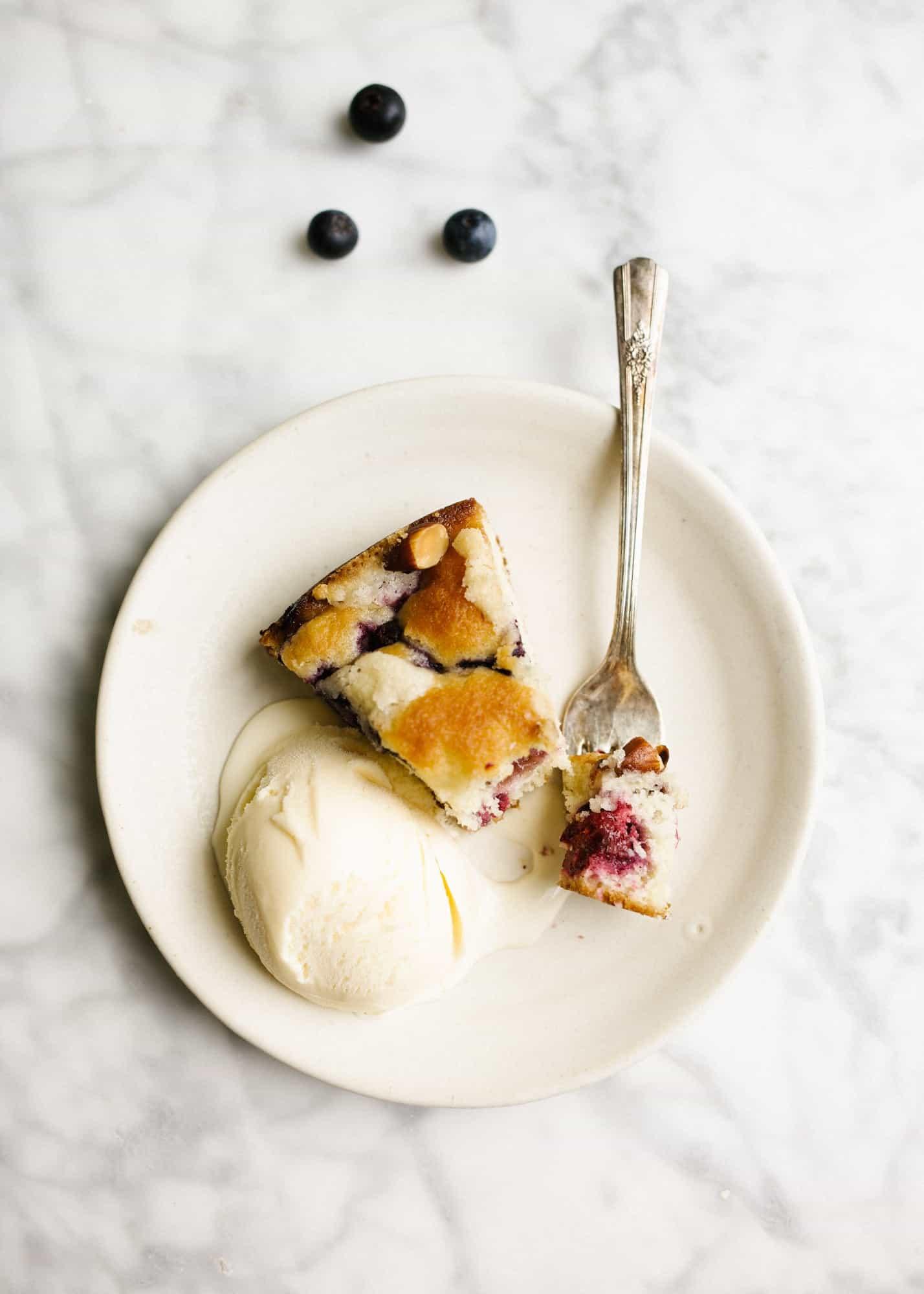 A close-up shot of a slice of Wild Berry Buckle with a scoop of vanilla ice cream on a plate
