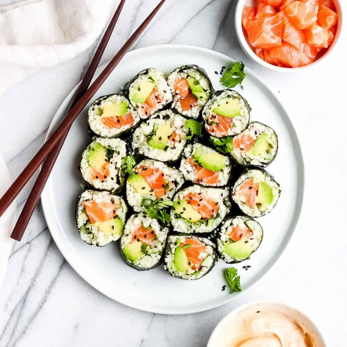 A platter of finished cauliflower rice sushi rolls, garnished with sesame seeds