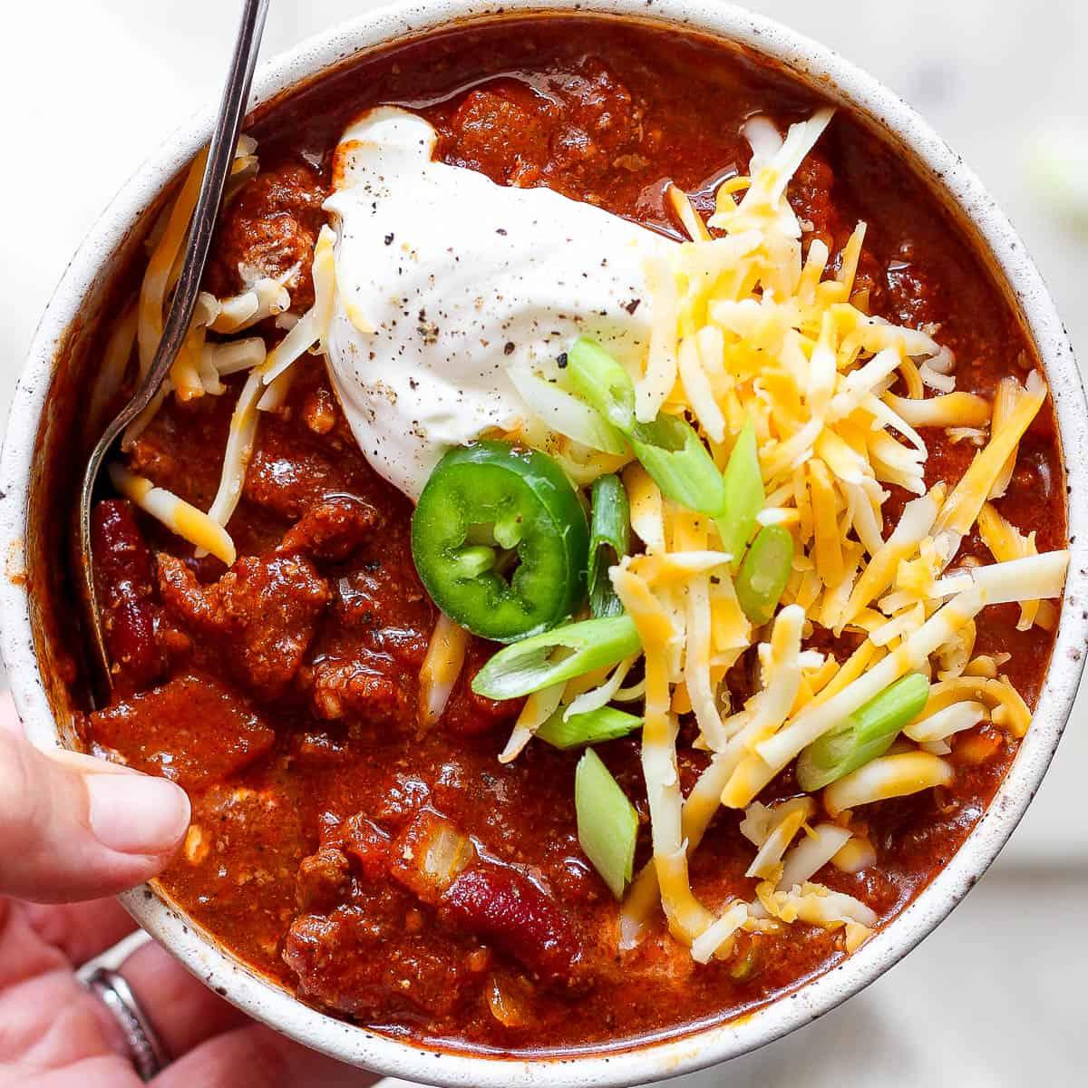 A hearty bowl of Smoked Colby Jack Chili, garnished with green onions and a dollop of sour cream, with a smoky background.