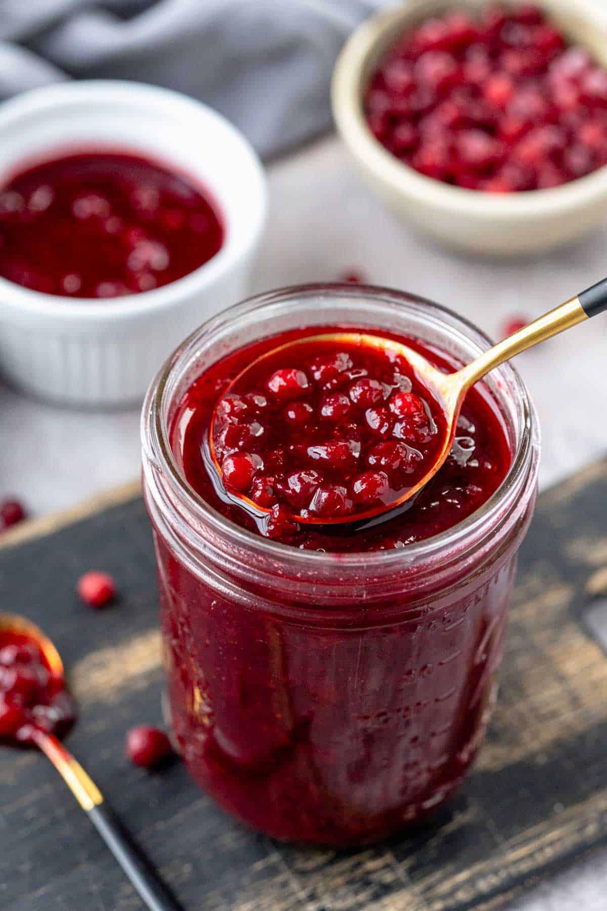 A jar of homemade lingonberry jam next to a bowl of cranberry sauce