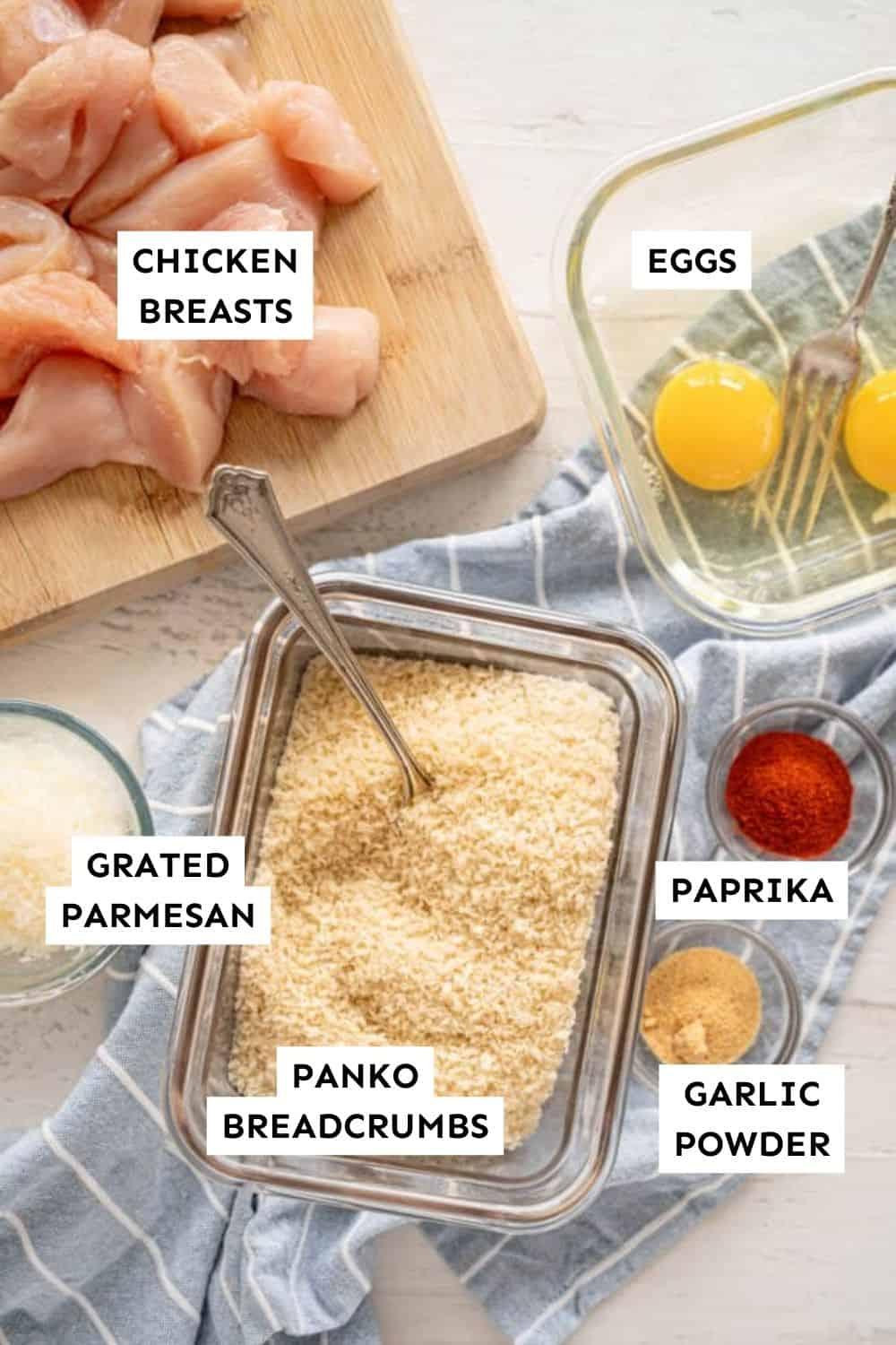 ingredients for the pirate treasure chicken nuggets, including chicken breasts, breadcrumbs, eggs, flour, and spices arranged on a wooden cutting board