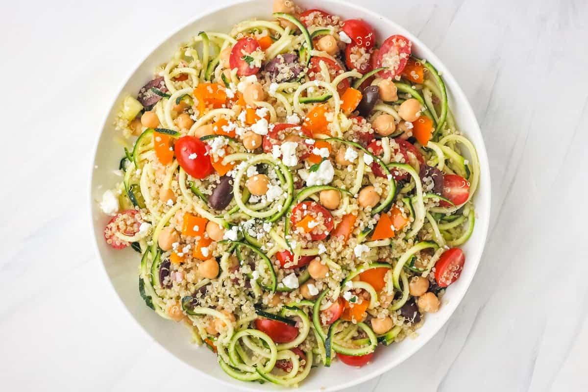 A wide shot of a person serving the zucchini noodles and Mediterranean quinoa salad.