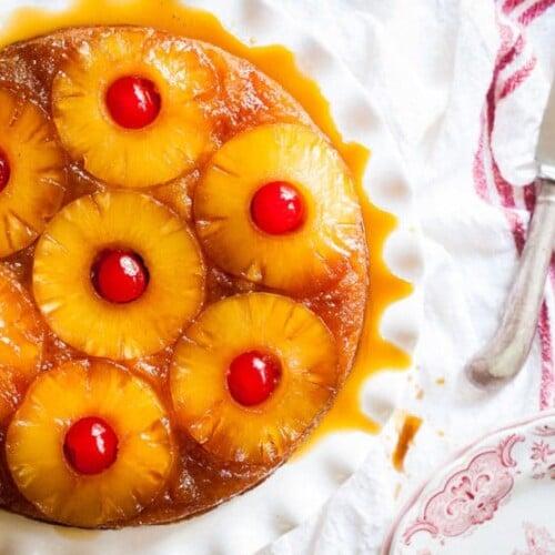 A golden-brown pineapple upside-down cake, glistening with caramelized sugar and juicy pineapple slices, served on a plate.
