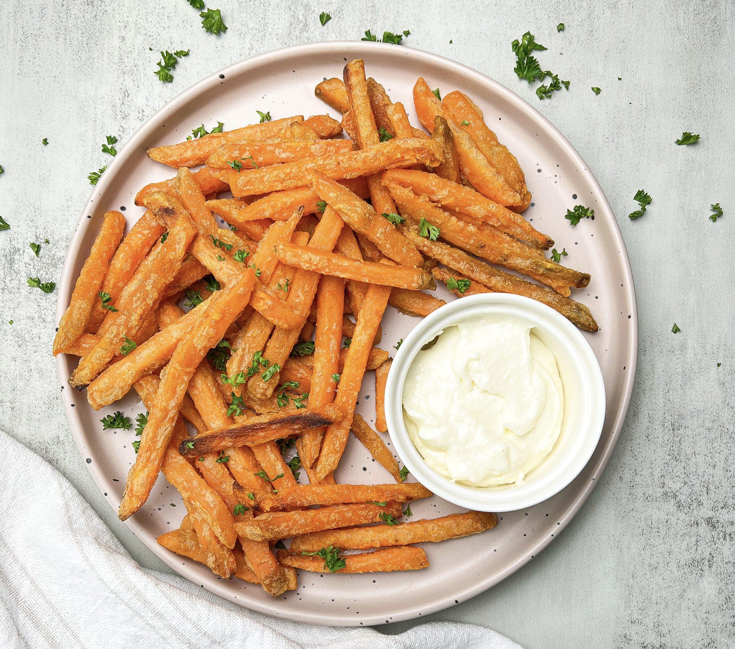 Close-up of a hand dipping a sweet potato fry into a bowl of garlic aioli.