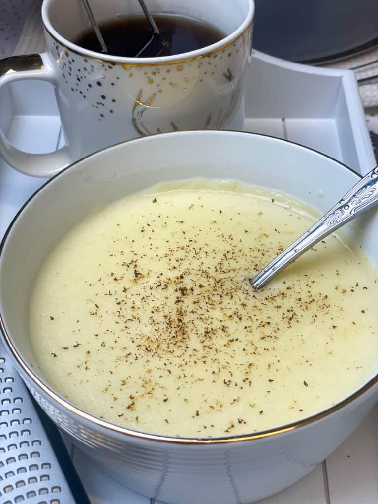 A bowl of wheat and semolina pudding next to a steaming mug of tea