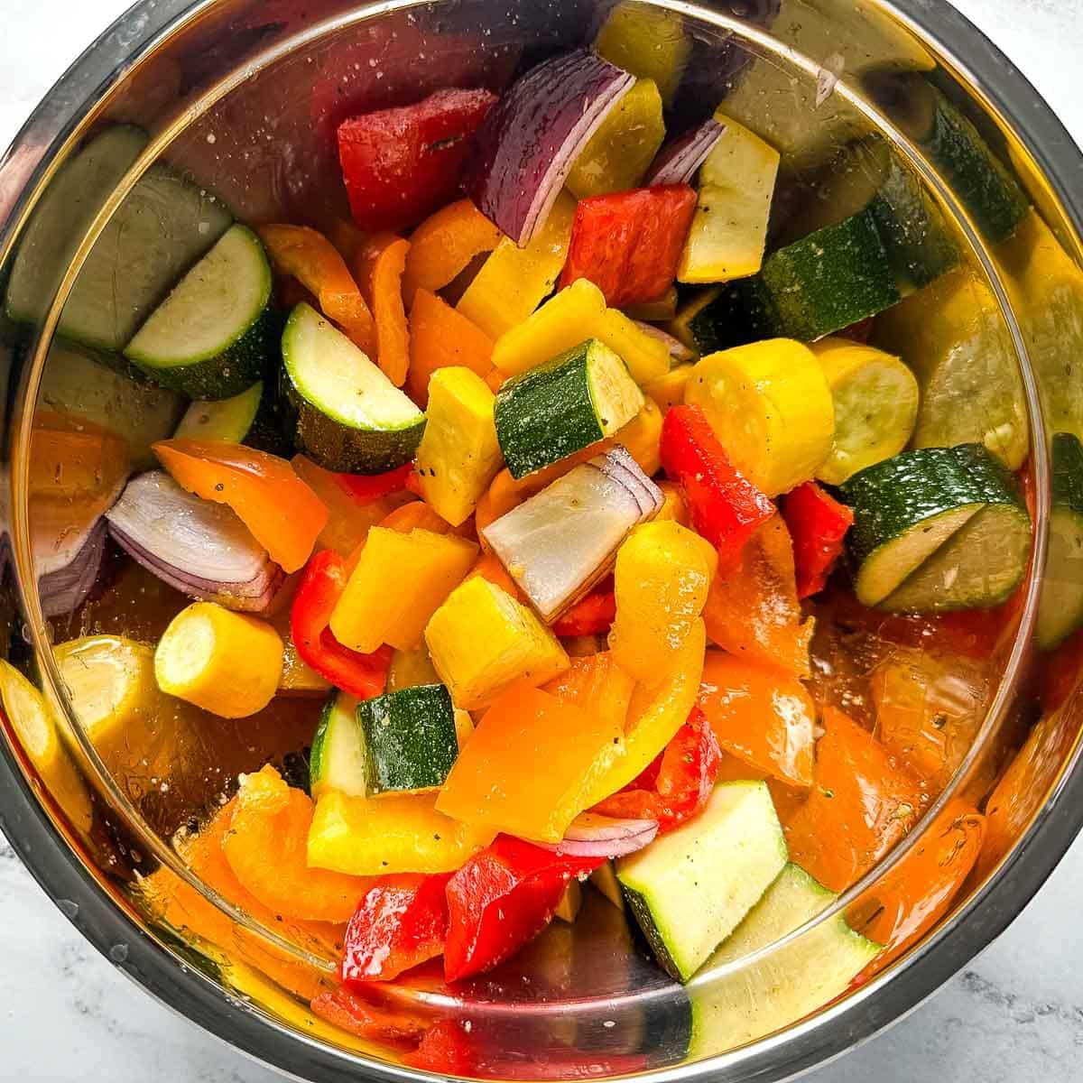 close-up of roasted vegetables being tossed in a bowl with olive oil