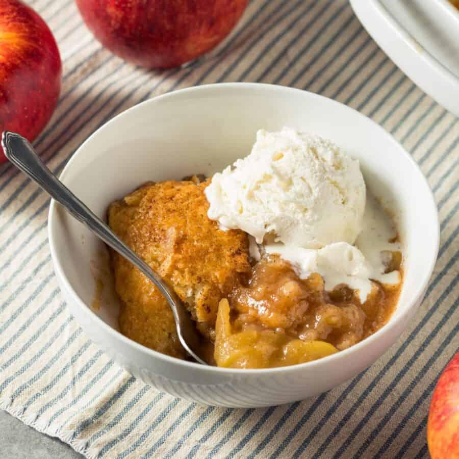 A rustic, golden-brown apple crisp cobbler in a baking dish, garnished with a scoop of vanilla ice cream