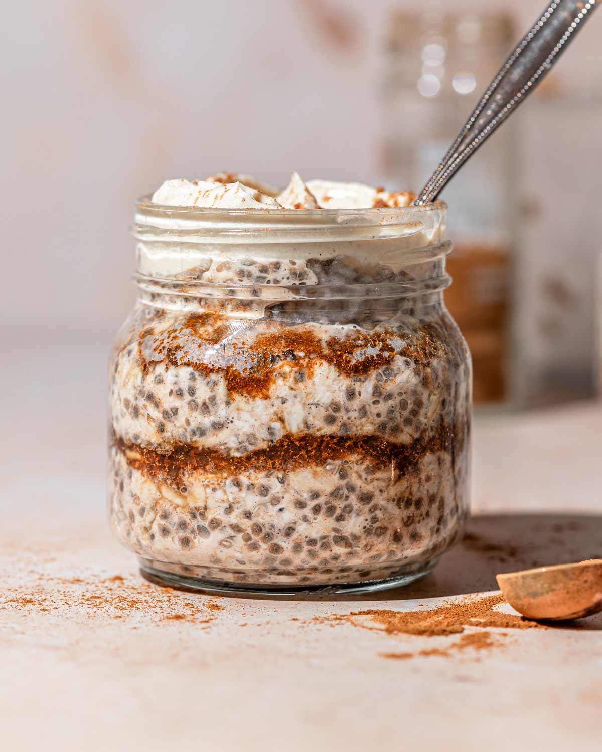 Close-up shot of a jar filled with creamy cinnamon roll overnight oats, showing layers of oats and a cinnamon swirl topping