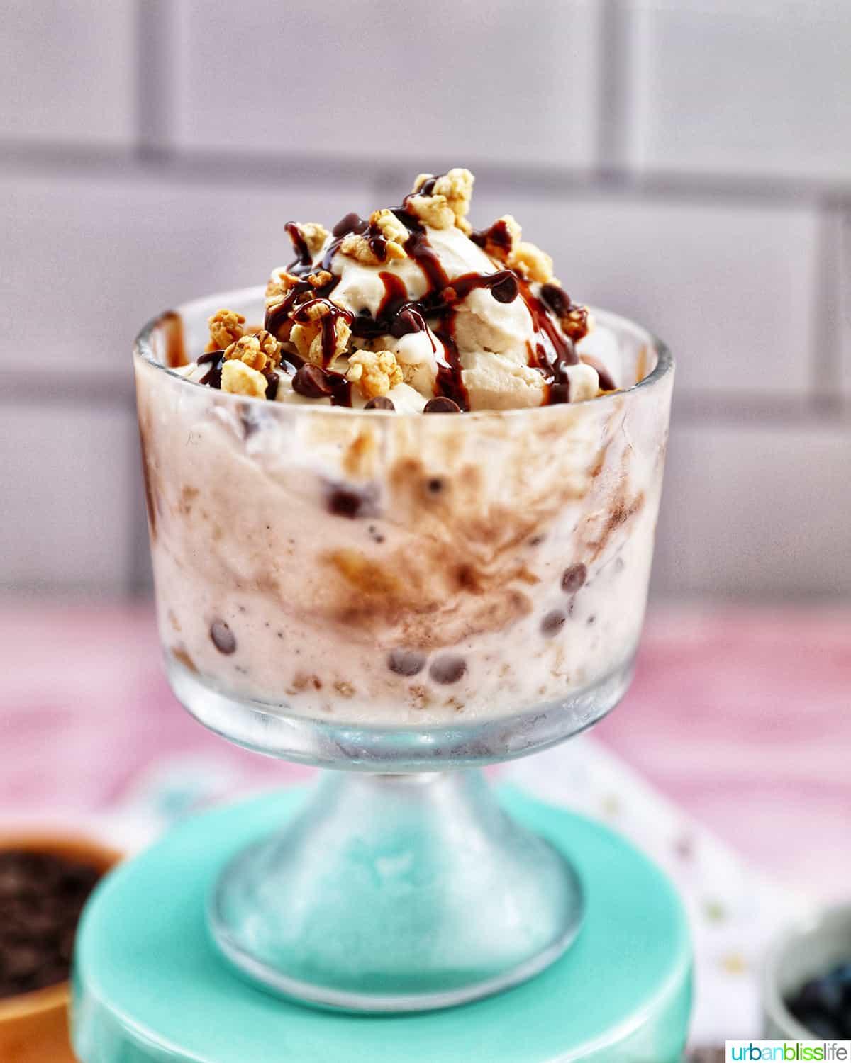 Close up shot of layered ice cream parfait in a clear cup with cookie crumbs, chocolate syrup, and strawberries.