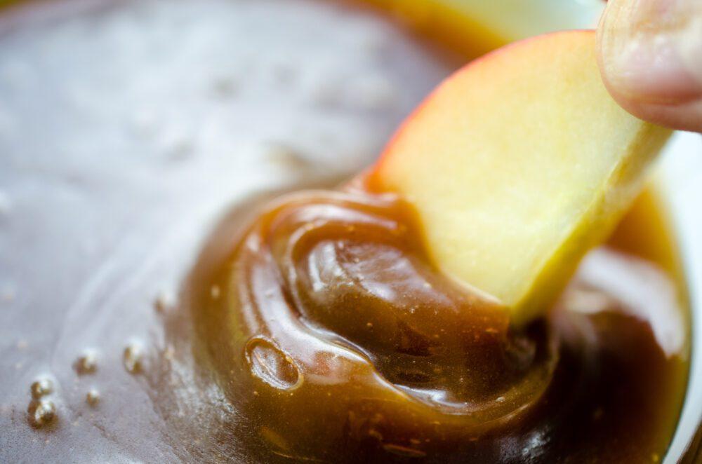 A bowl of homemade caramel dip with a spoon next to it.