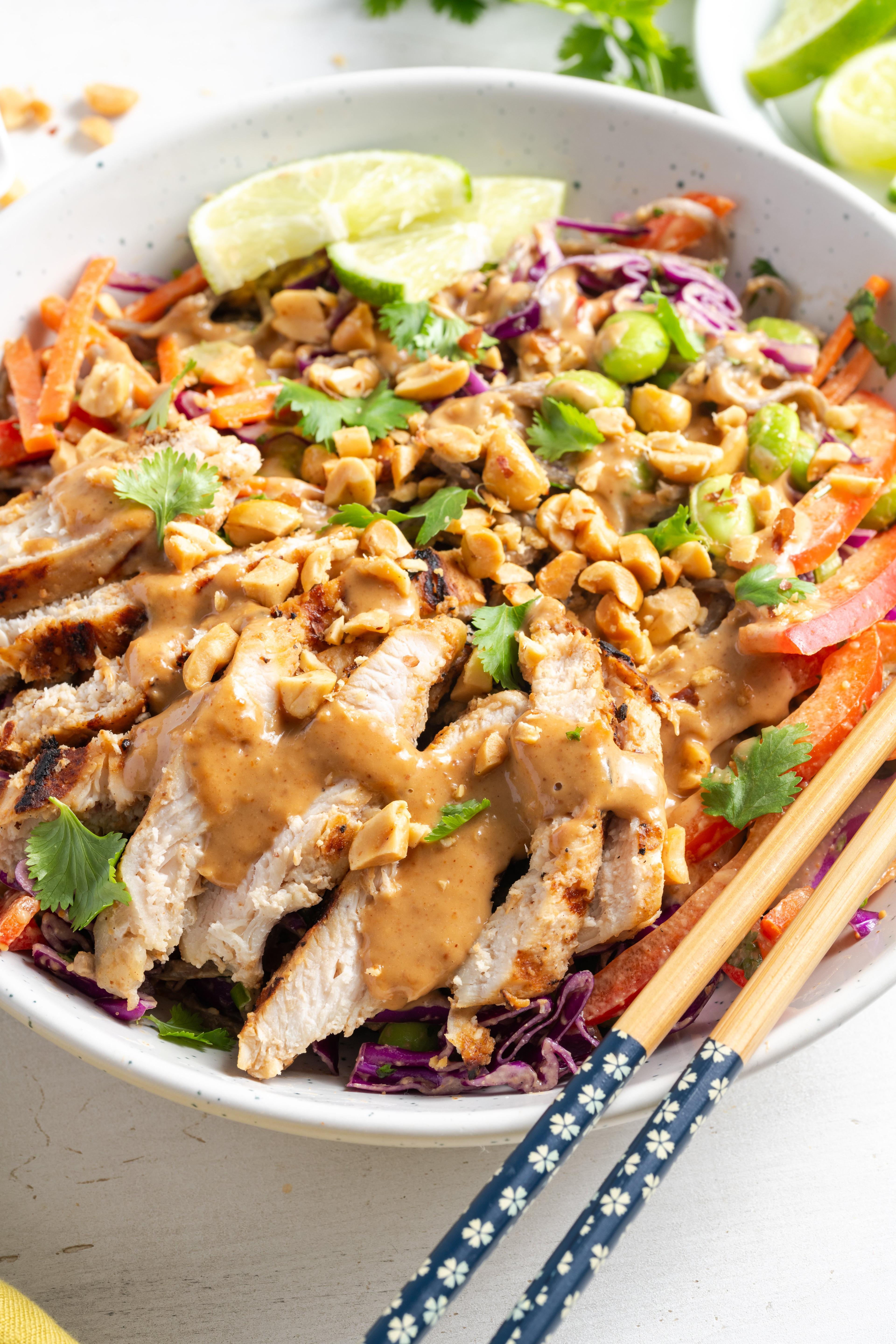 A person holding a Thai peanut noodle grain bowl with chicken, smiling