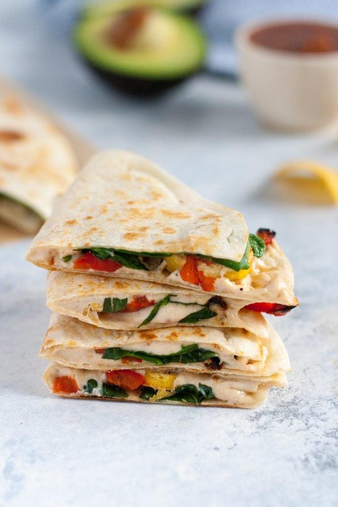 A person assembling a plantain quesadilla, adding cheese and peppers