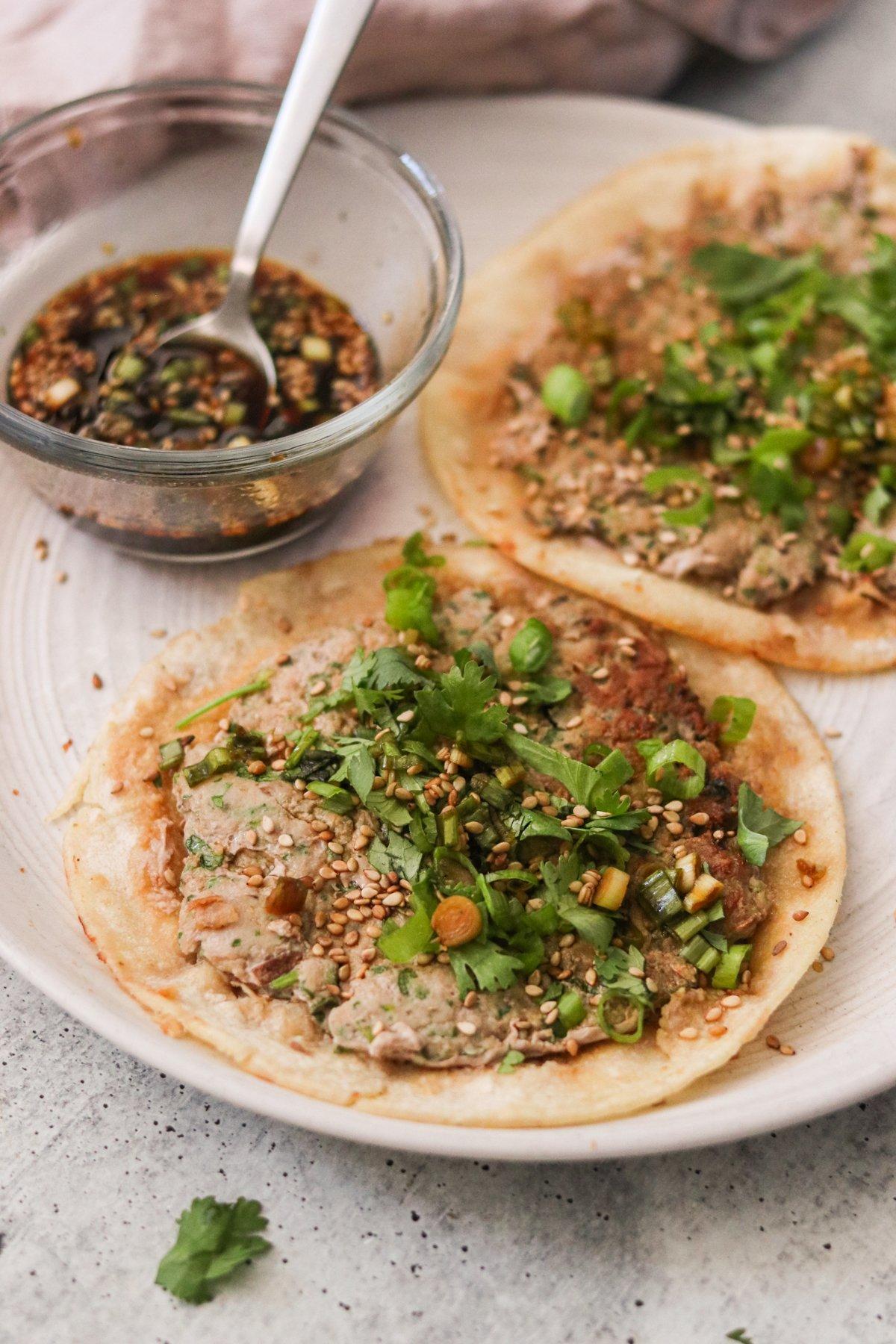 Close up of a plate of kimchi dumplings tacos with various toppings.