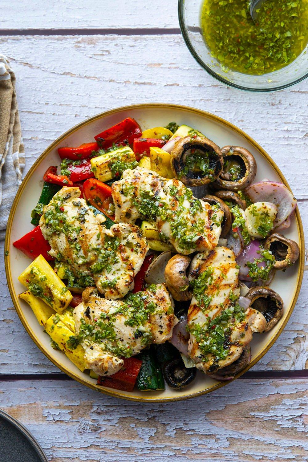 A table set for a summer meal, featuring grilled chicken with chimichurri sauce, and other side dishes