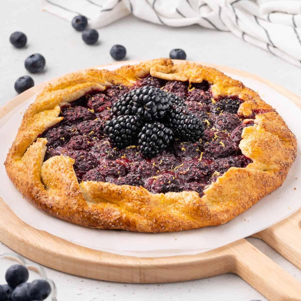 A rustic blackberry tart with balsamic glaze drizzled on top, garnished with fresh thyme sprigs