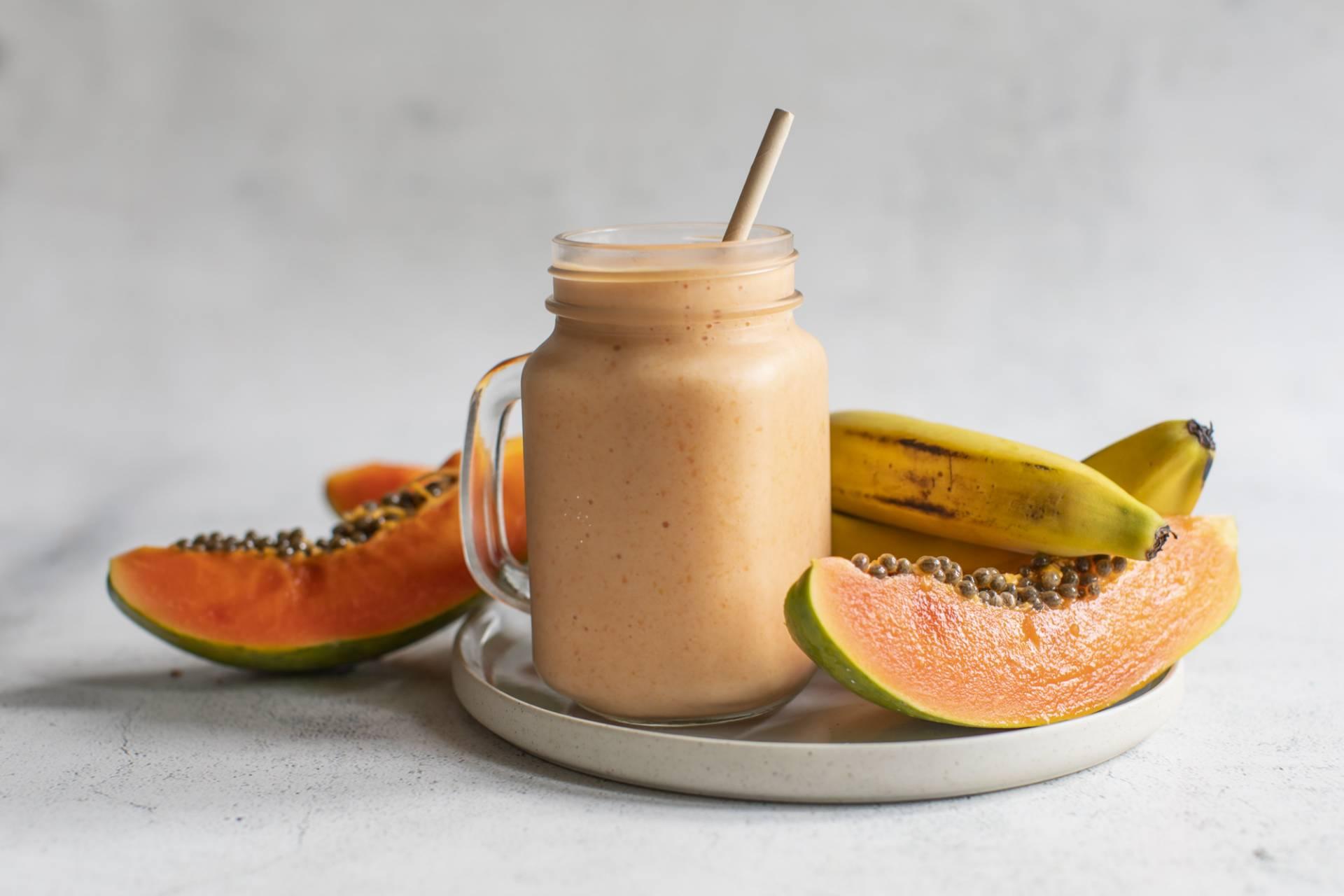 a person holding a banana and papaya smoothie outside on a sunny morning